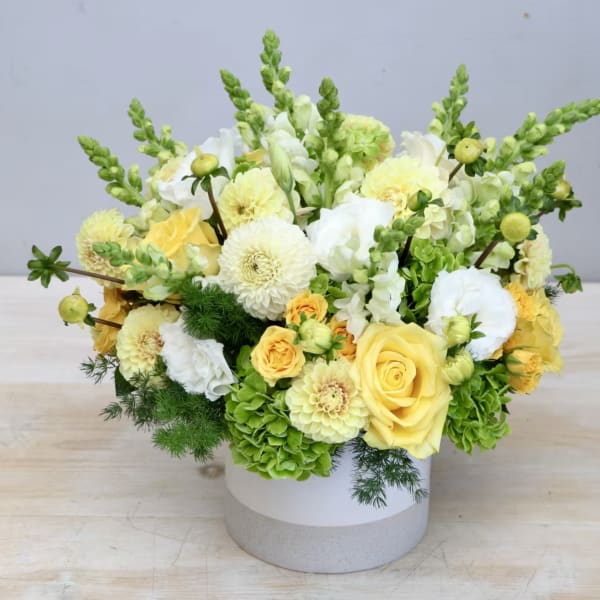 Yellow and white floral arrangement in a round white vase