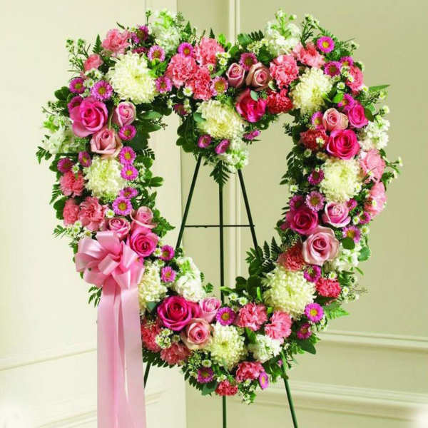 Heart-shaped standing wreath of pink roses, carnations, and white mums with bow on easel
