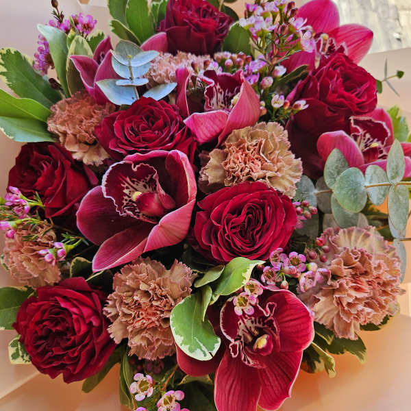 Bouquet of red roses, pink orchids, and carnations in pale wrapping