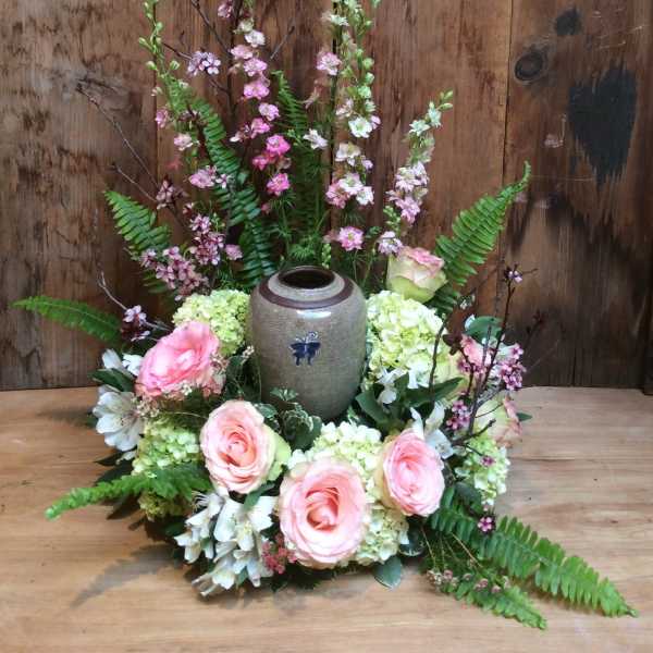 Pink roses and white flowers arranged around a ceramic urn
