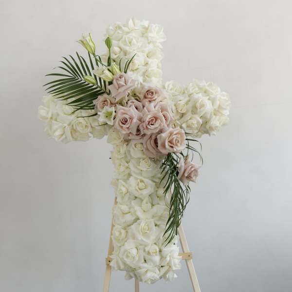 Cross-shaped floral arrangement of white and blush roses on an easel