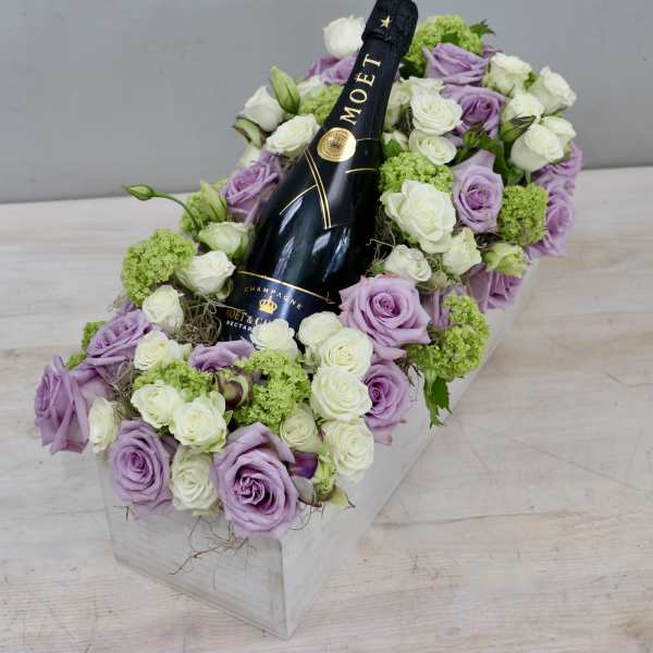 Lavender and white roses arranged around a champagne bottle in a white box