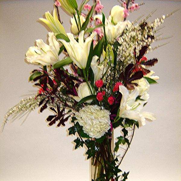 Tall bouquet of white lilies and mixed flowers in a clear glass vase