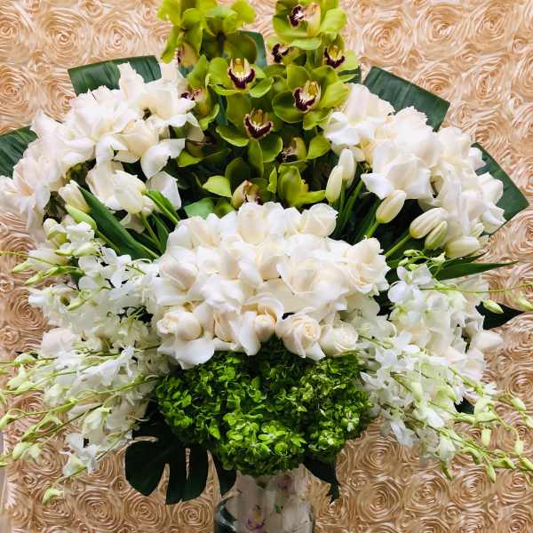 Tall white floral arrangement in a clear glass vase with green orchids