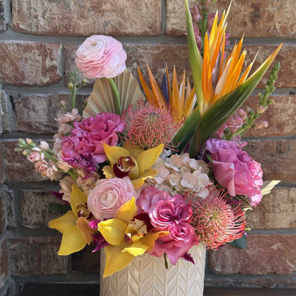 Bright tropical bouquet in a white textured vase with pink and yellow blooms