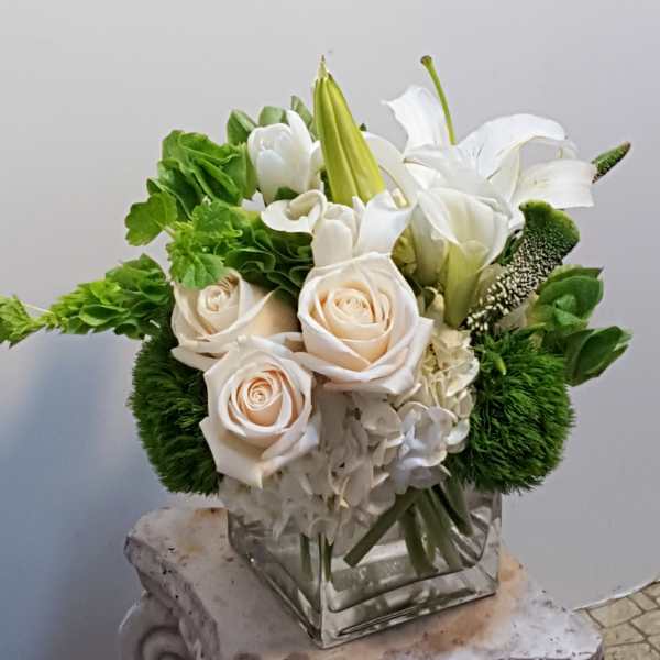 Compact arrangement of cream roses and white lilies in a clear glass cube vase