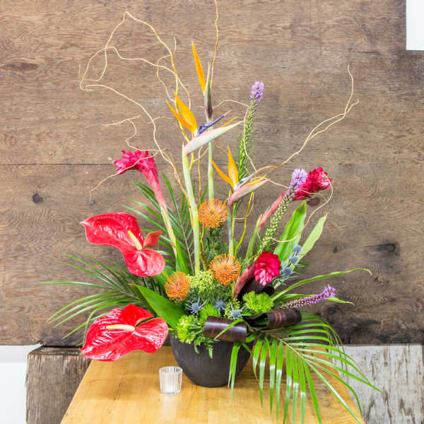 Tropical flower arrangement in a dark vase with red anthuriums and bird of paradise