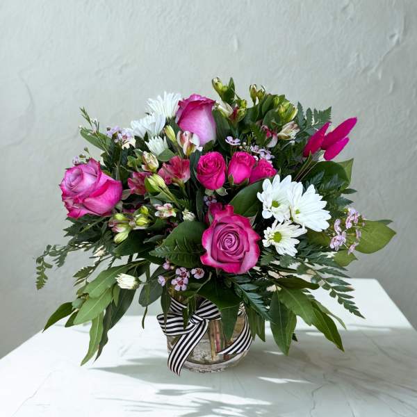 Pink roses and white daisies in a glass vase with a striped ribbon