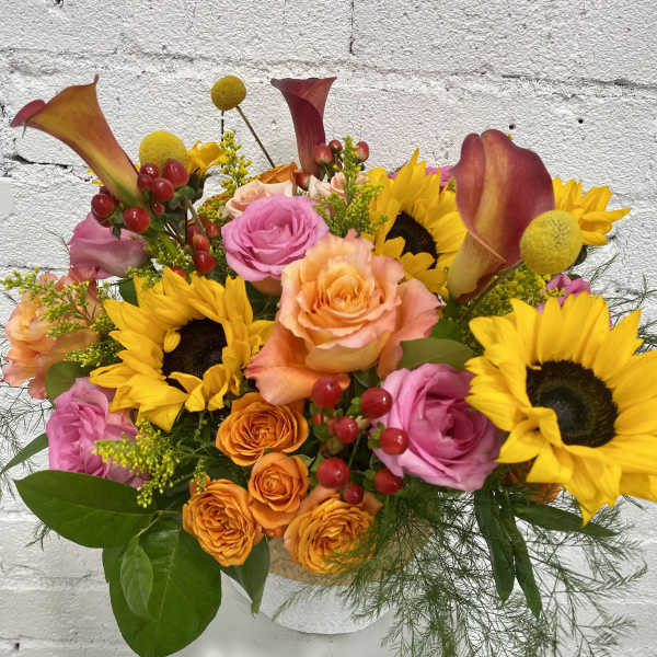 Mixed bouquet with sunflowers, roses, and calla lilies in a white vase