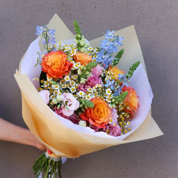 Hand-tied bouquet of orange roses, blue flowers, and small white daisies