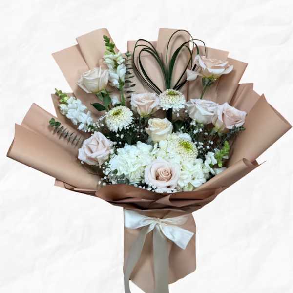 Bouquet of pale roses and white flowers wrapped in tan paper with a ribbon