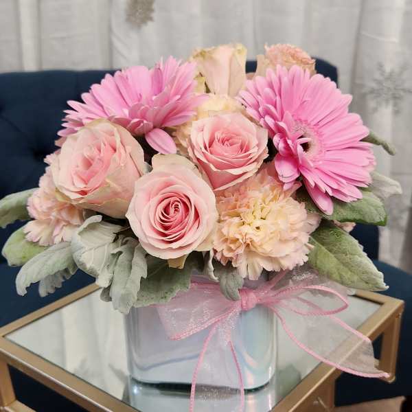 Pink roses and gerbera daisies in a clear glass vase with a pink ribbon