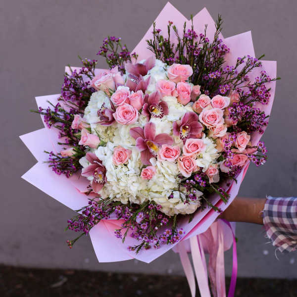 Pink roses and white hydrangeas in a wrapped bouquet with purple accents