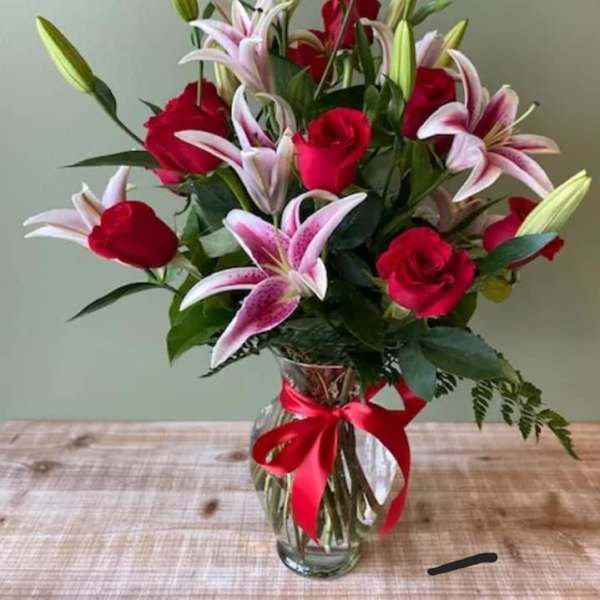 Red roses and pink lilies in a clear glass vase with a red ribbon