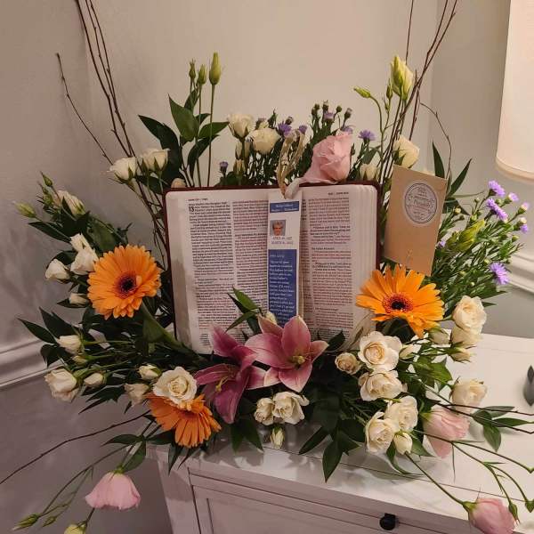 Floral sympathy arrangement around an open book with orange gerberas and pink lilies