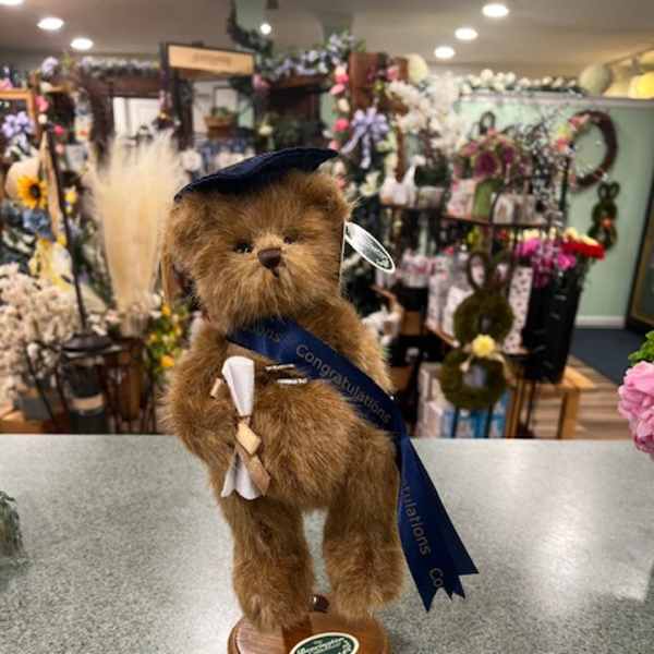 Plush teddy bear figurine on a wooden base with a graduation ribbon