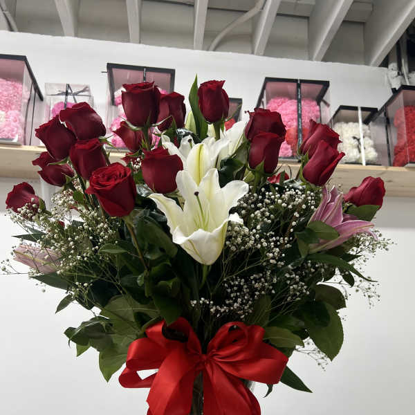 Tall bouquet of red roses and white lilies in a glass vase with a red ribbon