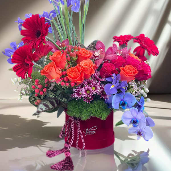 Mixed bouquet with orange roses, red gerberas, and purple orchids in a red hat box