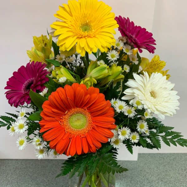 Mixed bouquet of bright gerbera daisies and small white daisies in a clear glass vase