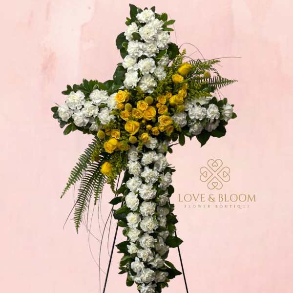 Cross-shaped floral tribute with white and yellow flowers on a stand