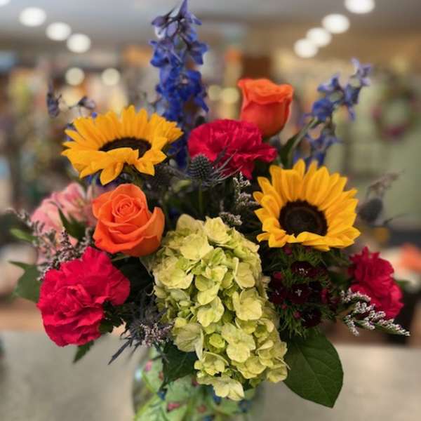 Mixed bouquet with sunflowers, roses, hydrangea, and carnations in a glass vase