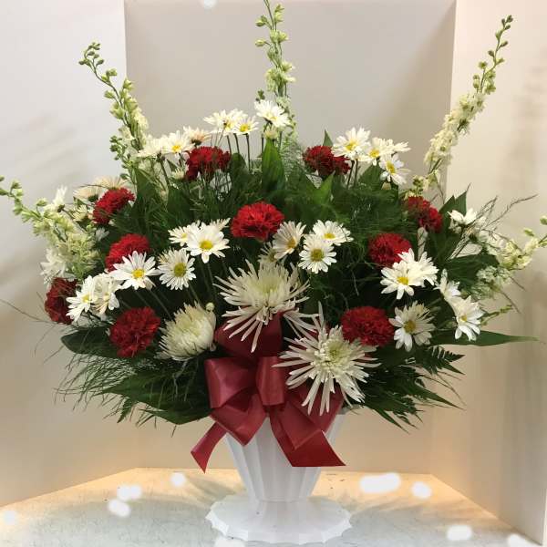Red and white flower arrangement in a white pedestal vase with a red ribbon