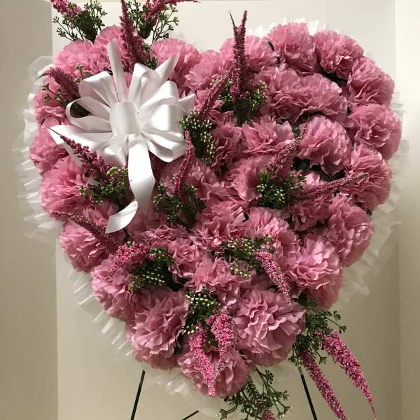 Heart-shaped pink carnation arrangement with a white ribbon bow