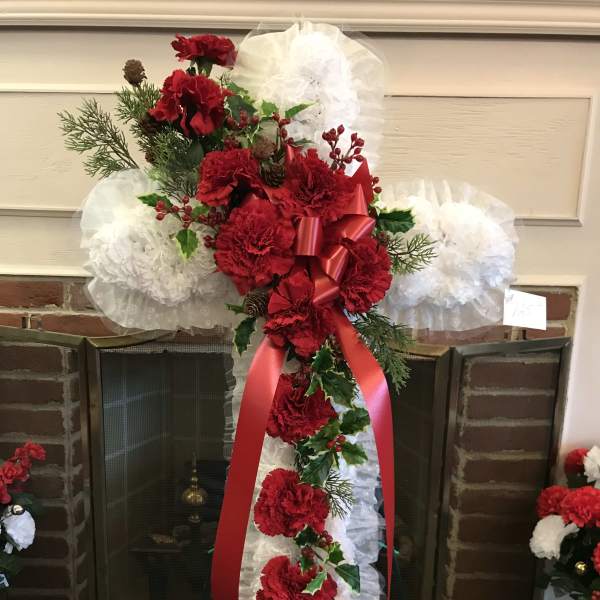Tall red carnation funeral spray with white ruffles and a red ribbon on an easel