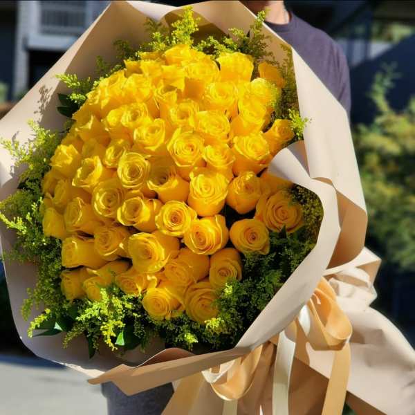 Large bouquet of yellow roses wrapped in beige paper with ribbon