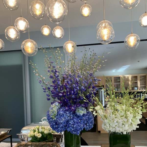 Tall blue and white floral arrangements in green glass vases