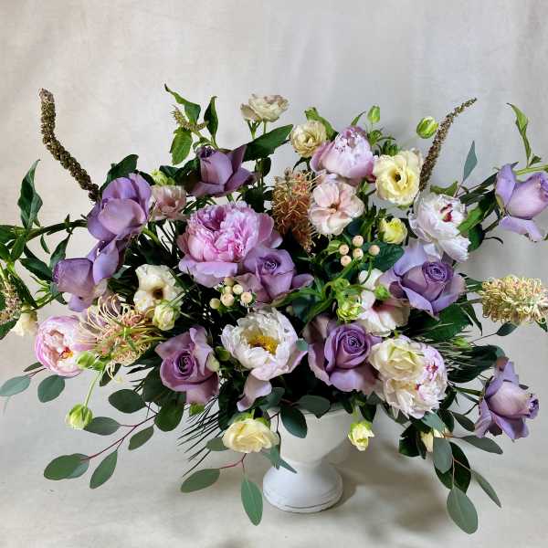 Lavender and white floral arrangement in a white pedestal vase