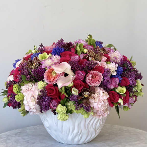 Large mixed bouquet in a white vase with pink, purple, and red blooms