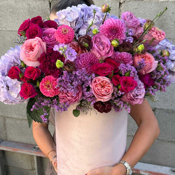 Large bouquet of pink, purple, and lavender flowers in a pale box