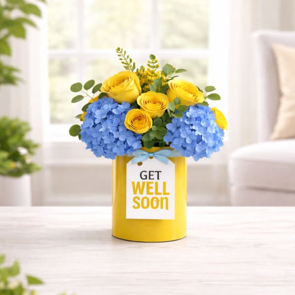 Yellow roses and blue hydrangeas in a yellow vase with a get well soon card
