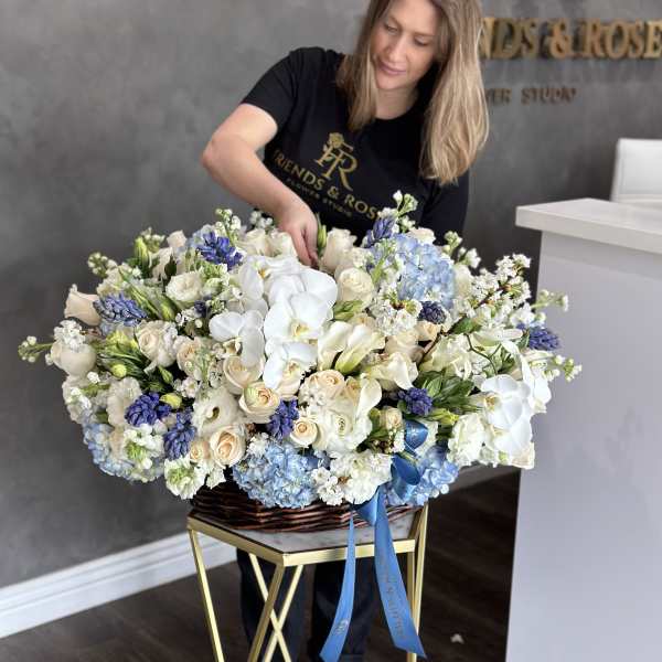 Large basket arrangement of white, cream, and blue flowers with a blue ribbon