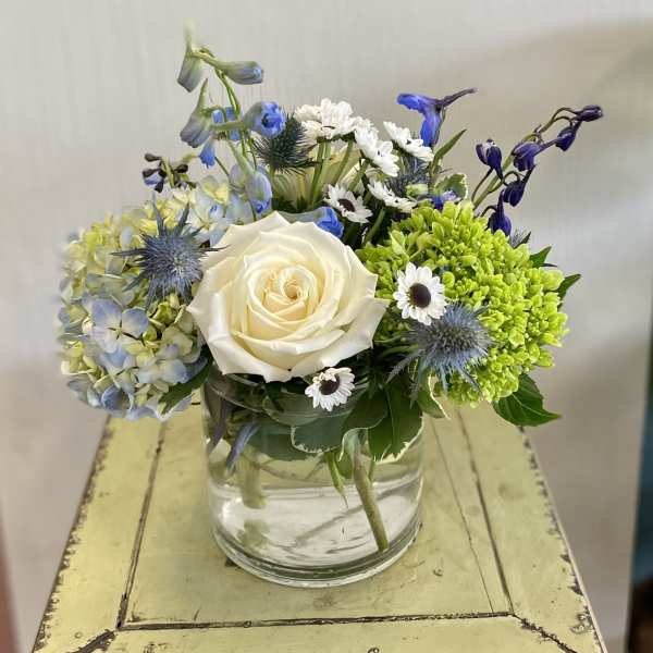 White rose arrangement with blue flowers in a clear glass vase