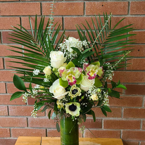 Tall floral arrangement with white roses and orchids in a green vase