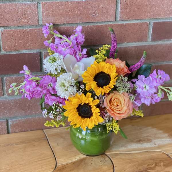 Mixed bouquet with sunflowers, roses, and purple blooms in a green vase