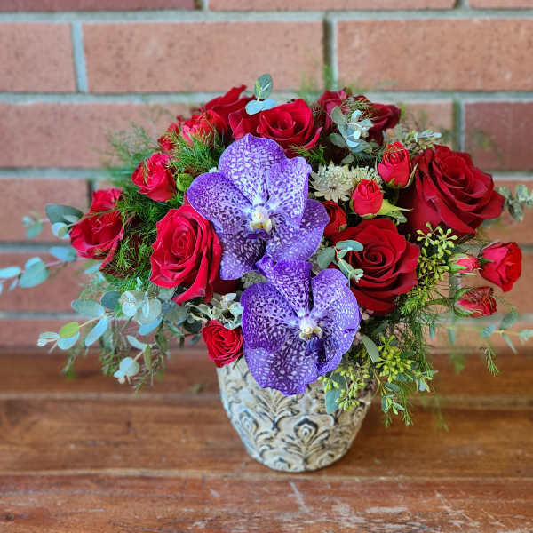 Red roses and purple orchids arranged in a decorative vase