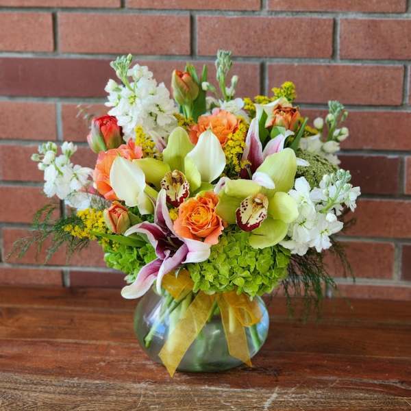Mixed bouquet in a glass vase with orange roses, orchids, and white blooms