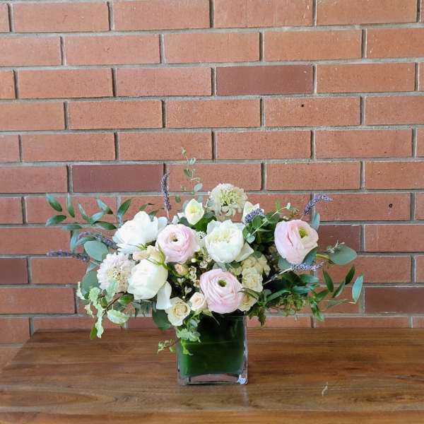 Low arrangement of white and pale pink flowers in a square glass vase lined with green inside