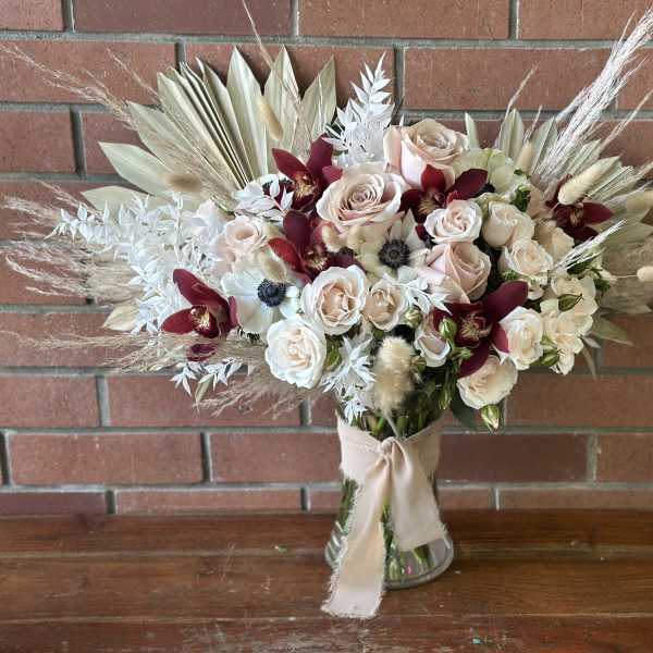 Bouquet of pale roses and burgundy orchids in a glass vase