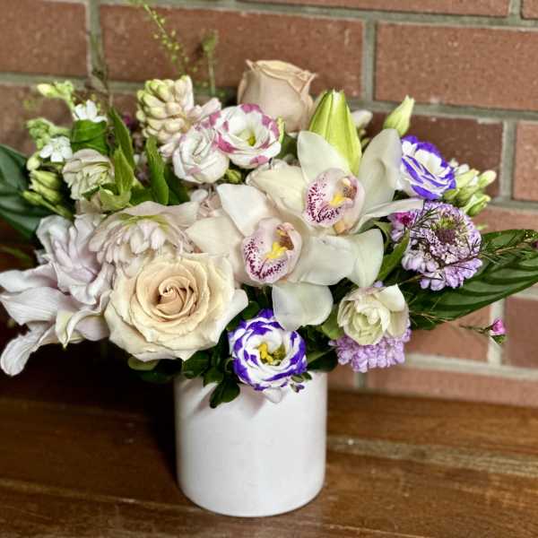 Mixed bouquet of cream, white, and purple flowers in a white vase