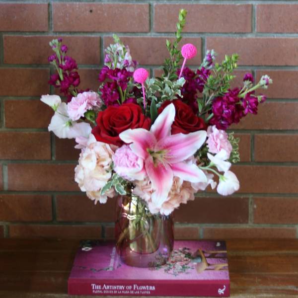 Pink and red floral arrangement in a glass vase on a book box