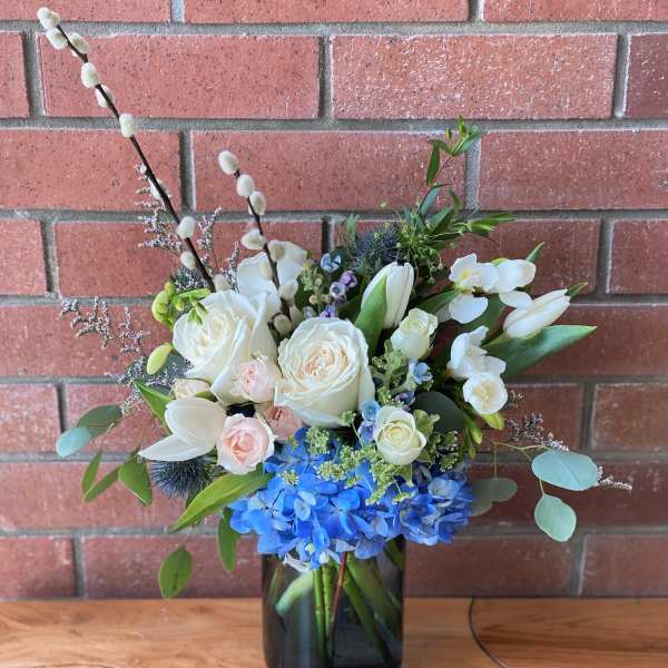 Vase arrangement of white roses, tulips, and blue hydrangeas with pussy willow branches