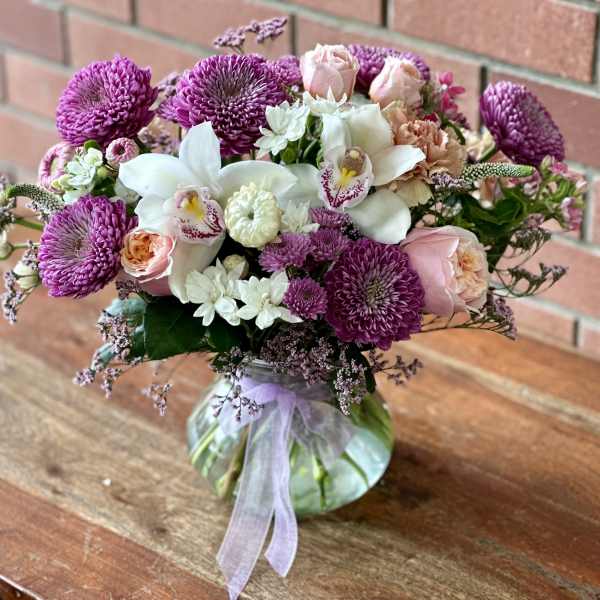 Bouquet of purple and pink flowers in a glass vase with a ribbon