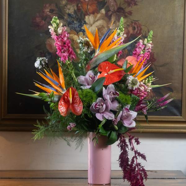 Tall tropical arrangement with orange birds of paradise, pink snapdragons and red anthuriums in a pink vase