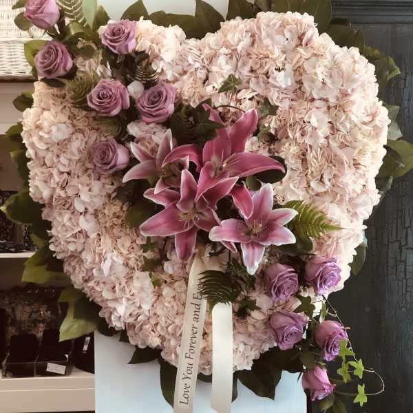 Heart-shaped floral arrangement with pink hydrangeas, purple roses, and lilies