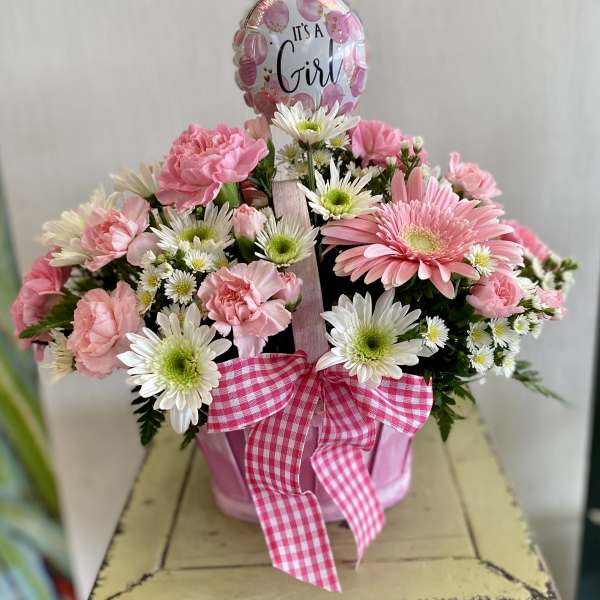 Pink and white flower arrangement in a pink container with a "It's a Girl" balloon