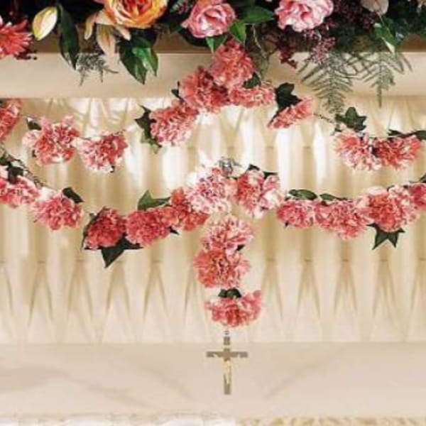 Pink floral garlands draped over a white draped backdrop with a hanging cross